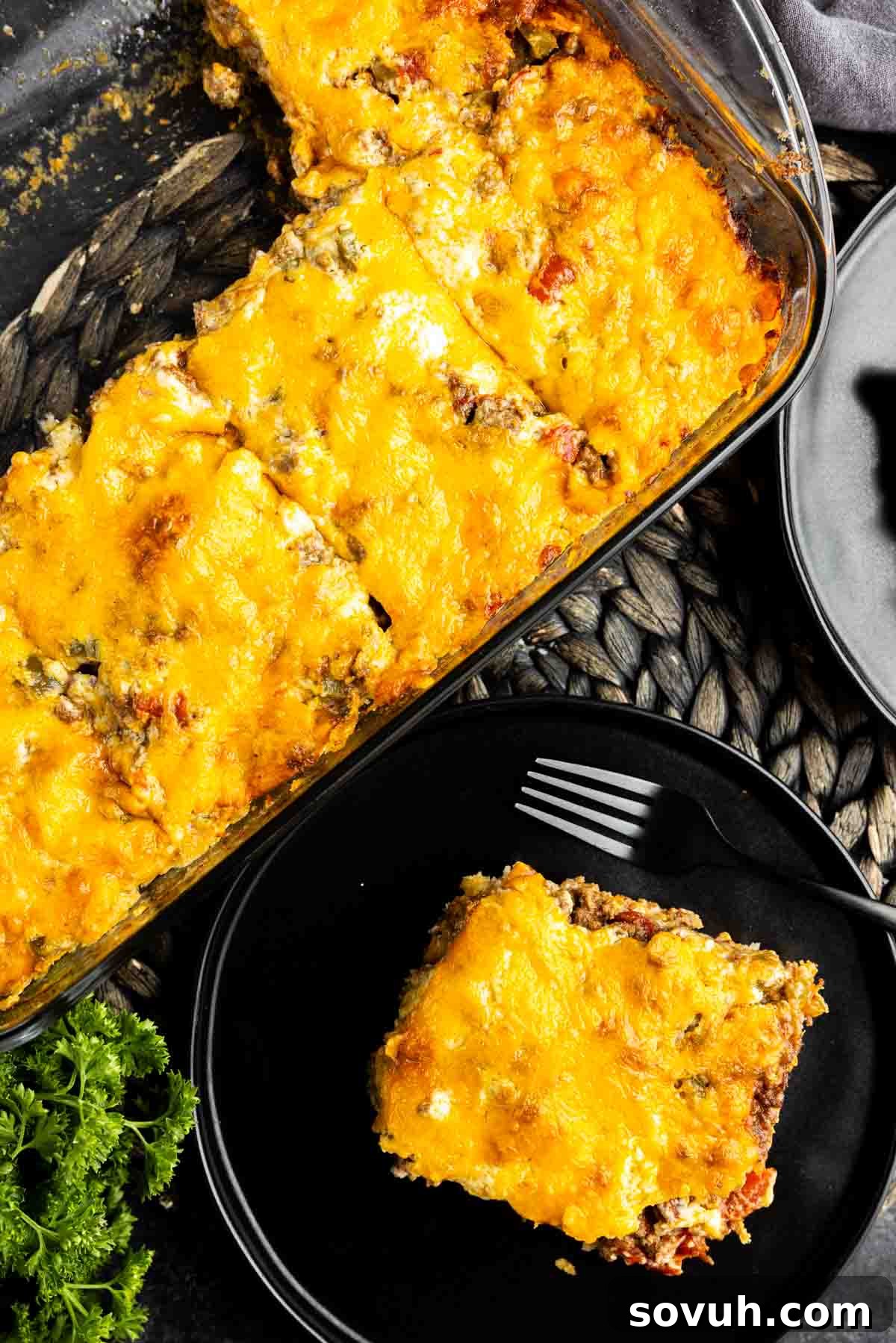 A casserole dish with a single, perfectly cut slice of John Wayne Casserole on a white plate, accompanied by a fork, ready to be eaten.
