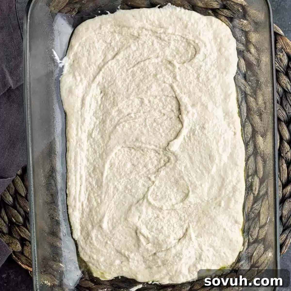 A baking dish with a uniform layer of Bisquick dough spread across the bottom, ready for the next layers of the John Wayne Casserole.