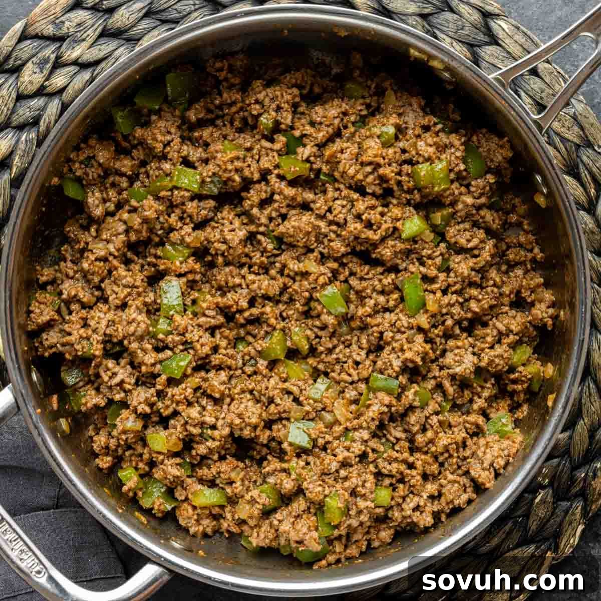 A skillet filled with browning ground beef and green peppers, actively cooking for the John Wayne Casserole filling.
