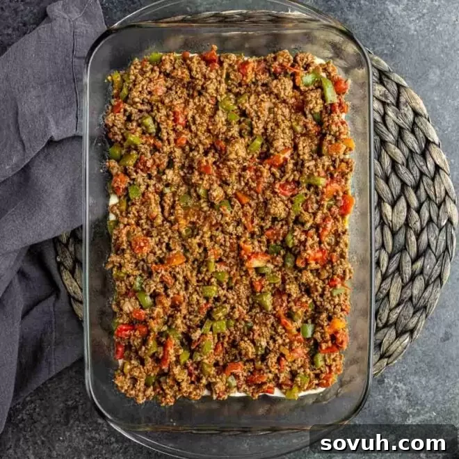 A glass baking dish with the biscuit base covered by a generous layer of seasoned ground beef and vegetables for the John Wayne Casserole.