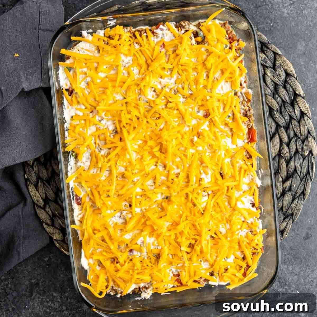 The assembled John Wayne Casserole, topped with a generous layer of shredded cheddar cheese, ready to be baked to perfection.