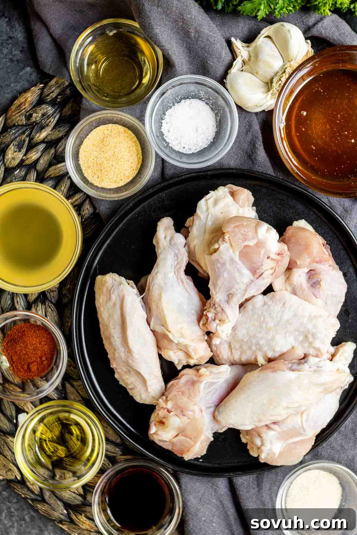 Ingredients for Honey Garlic Chicken Wings laid out on a black surface with spices and seasonings.