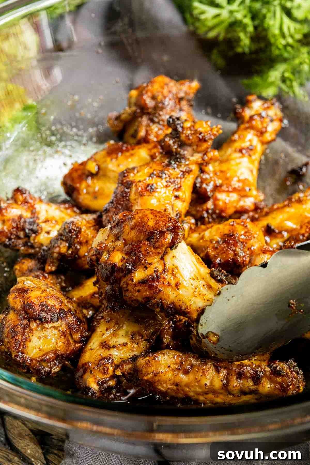Honey Garlic Chicken Wings in a glass bowl being tossed with tongs, coated in sauce.
