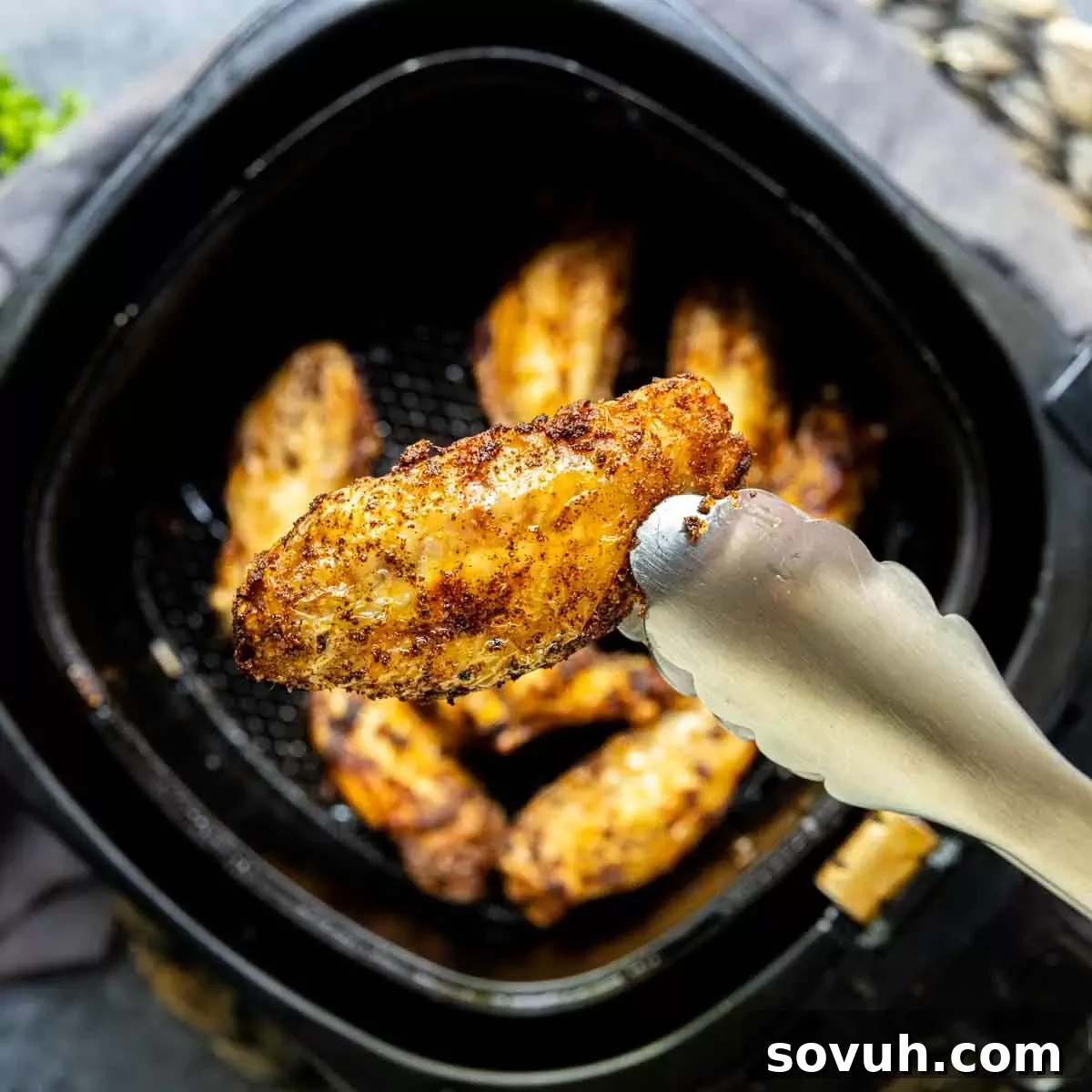 Golden-brown Frozen Chicken Wings being removed from an air fryer basket with tongs.