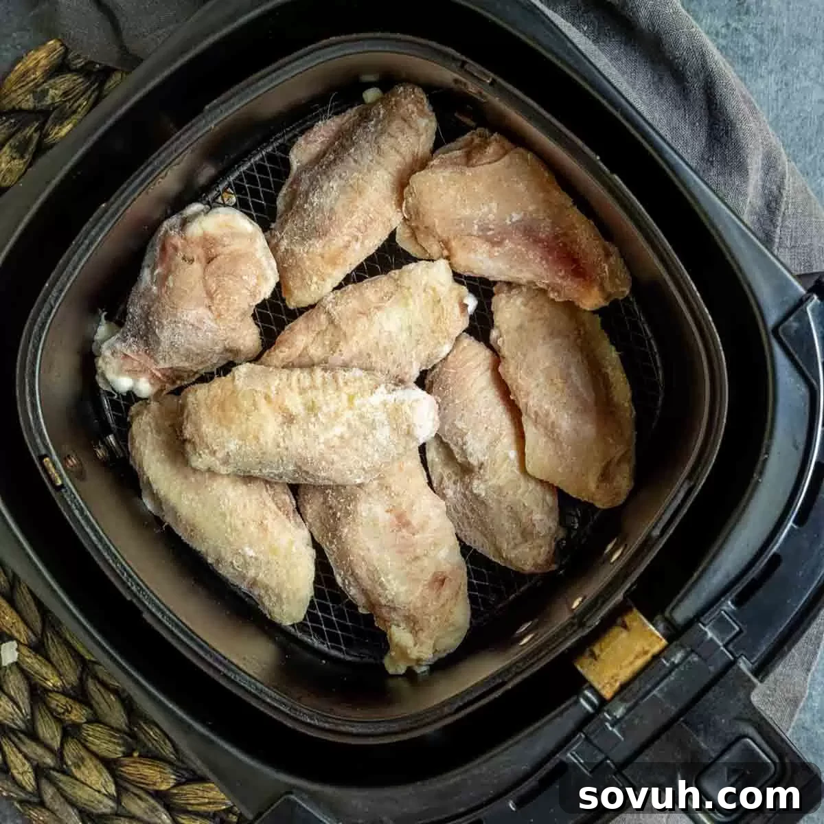 Frozen raw chicken wings placed in a single layer in an air fryer basket.