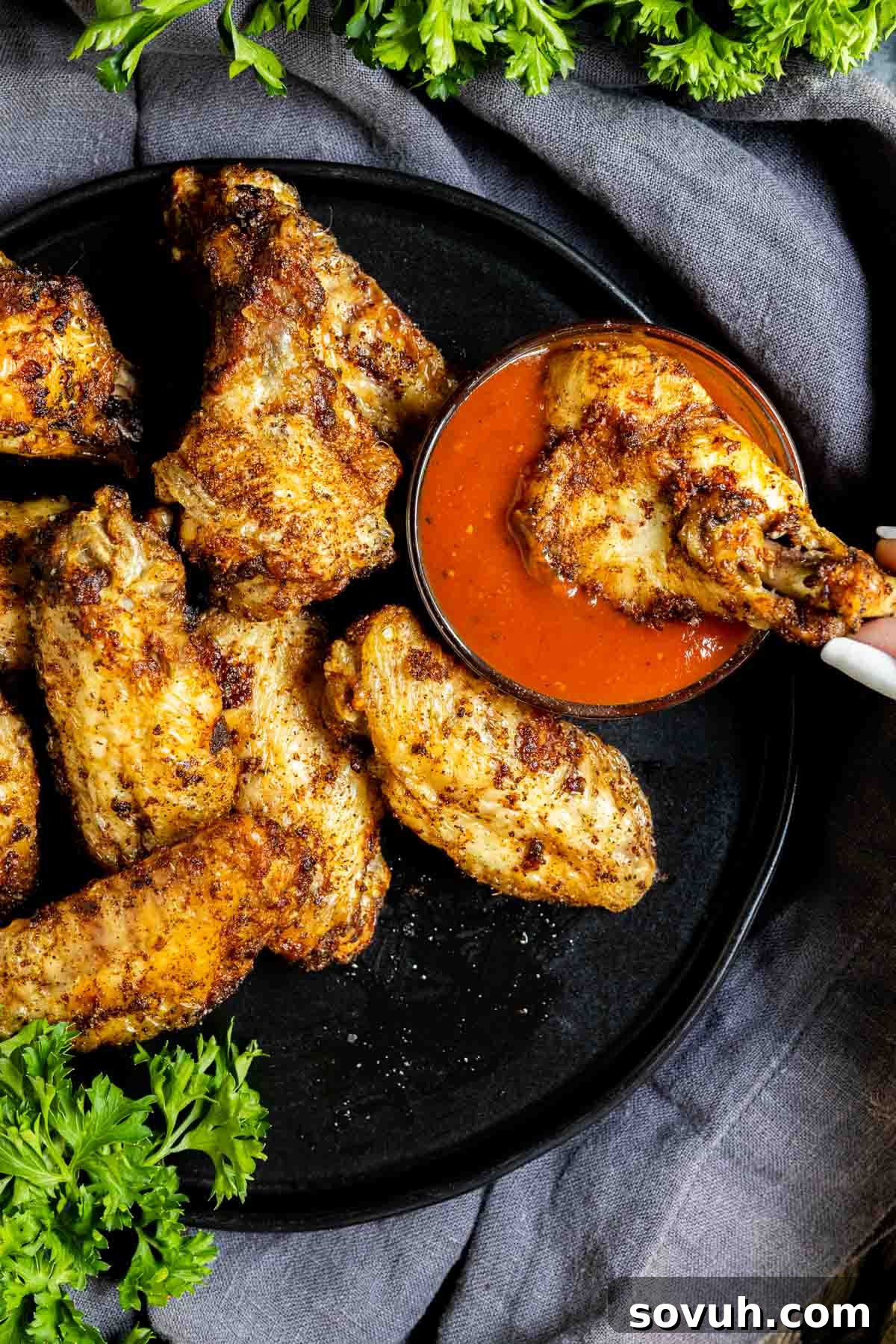 Air-fried frozen chicken wings on a plate, garnished with sauce and fresh parsley.