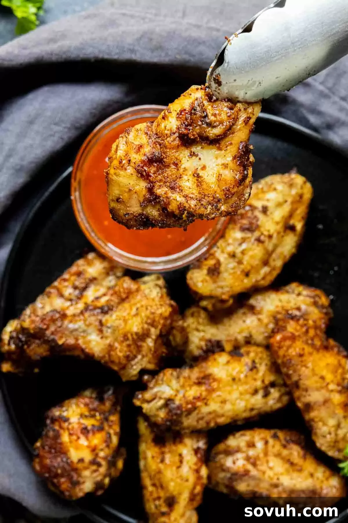 A crispy air-fried chicken wing being dipped into a sauce on a black plate.