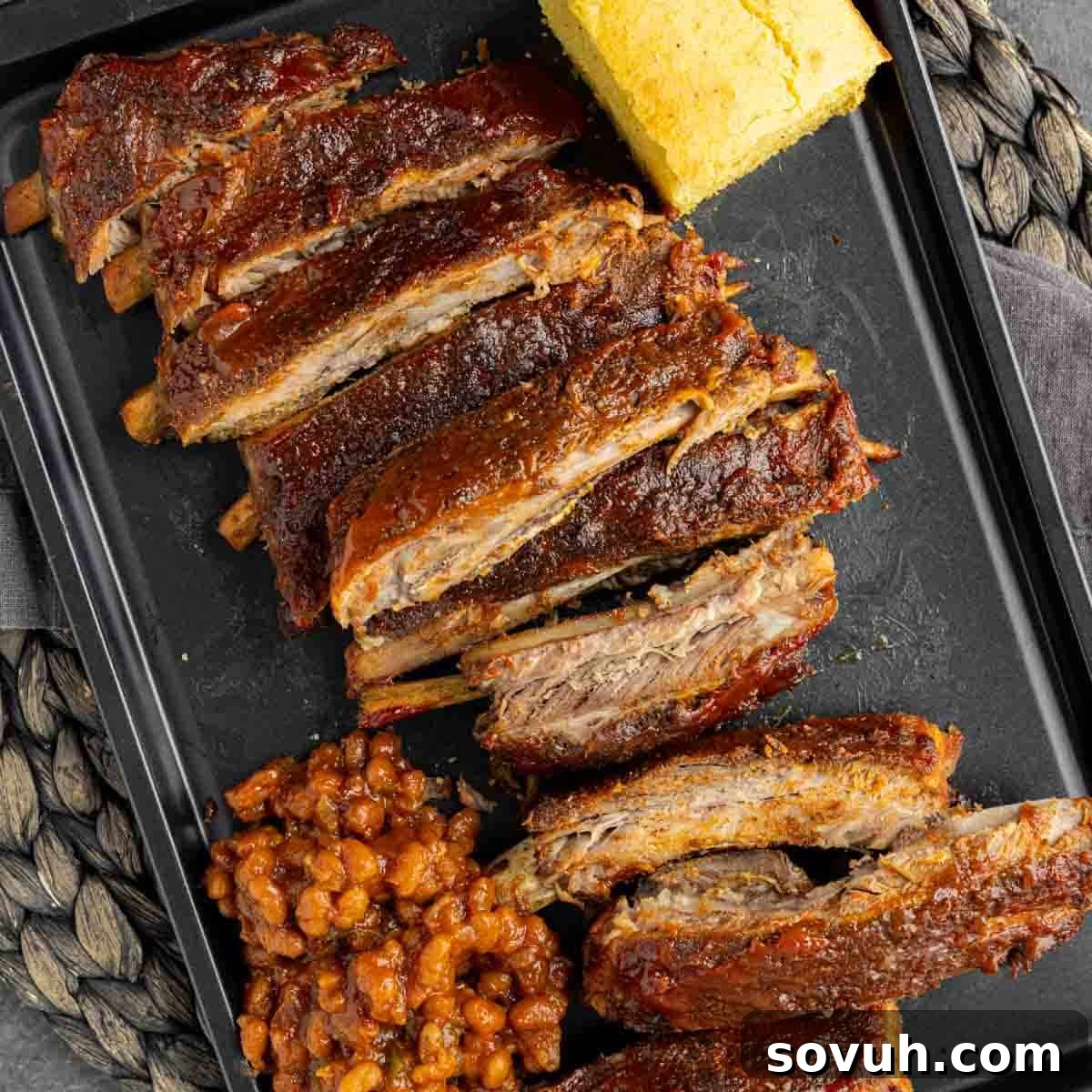 Sliced St Louis-Style Ribs on a black plate with cornbread and baked beans, viewed from above.