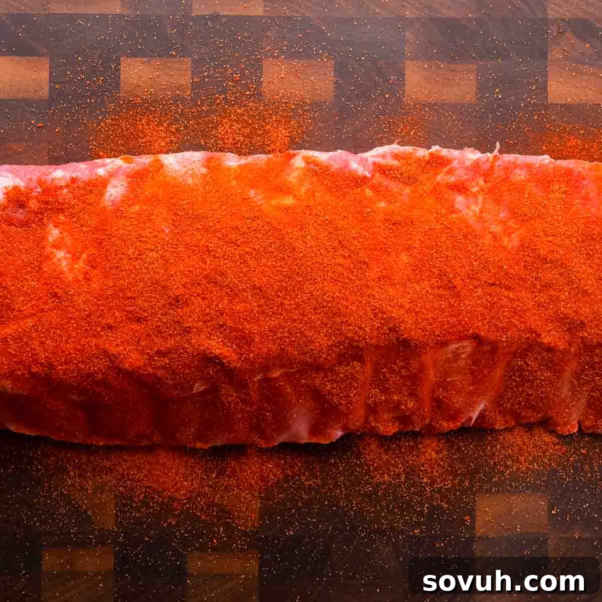 A raw St Louis-Style Ribs heavily coated with red spice rub on a wooden cutting board.