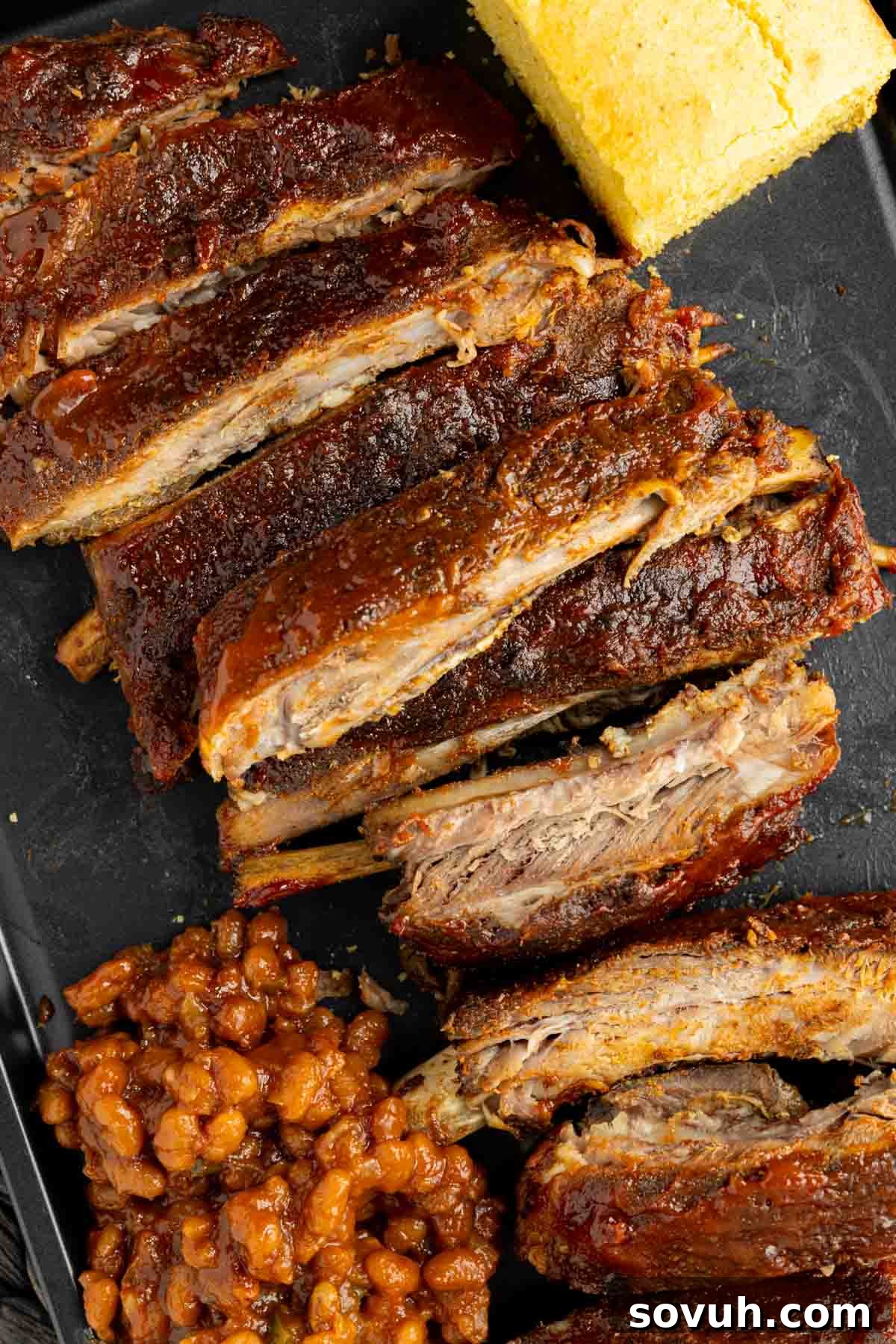 Sliced St Louis-Style Ribs served with cornbread and baked beans on a black plate.