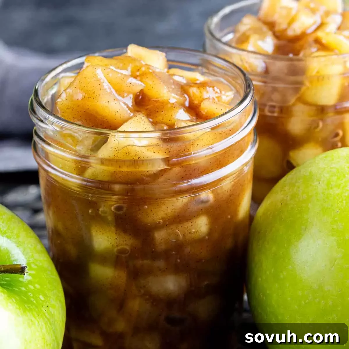 Two jars of homemade apple pie filling on a wooden table, garnished with cinnamon sticks and fresh apples.