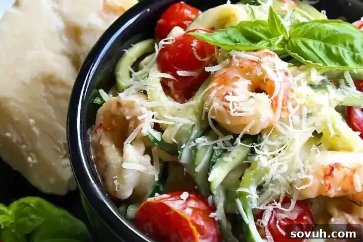 A bowl of shrimp pasta topped with halved cherry tomatoes, grated cheese, and fresh basil leaves. A block of cheese is visible in the background.