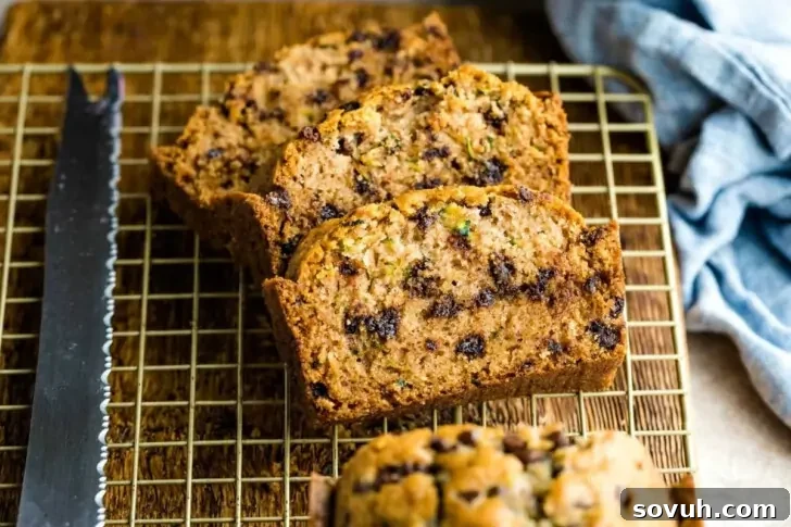 Slices of zucchini bread with chocolate chips on a cooling rack next to a serrated knife.