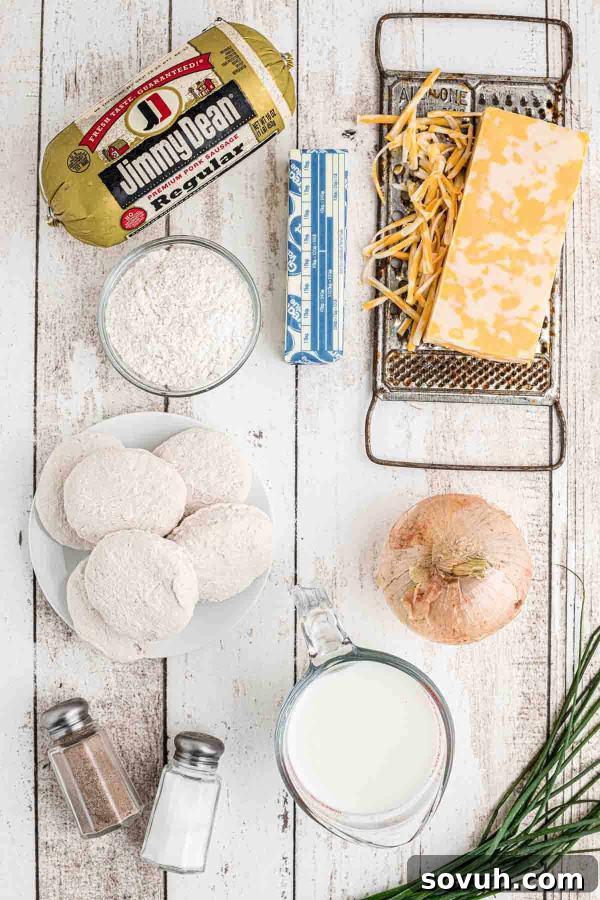 A table laden with fresh ingredients for a Biscuits and Gravy Casserole, including sausage, onions, milk, butter, and cheese.
