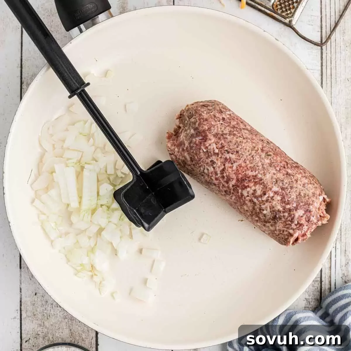 Sausage and diced onions cooking in a large skillet, browning evenly.