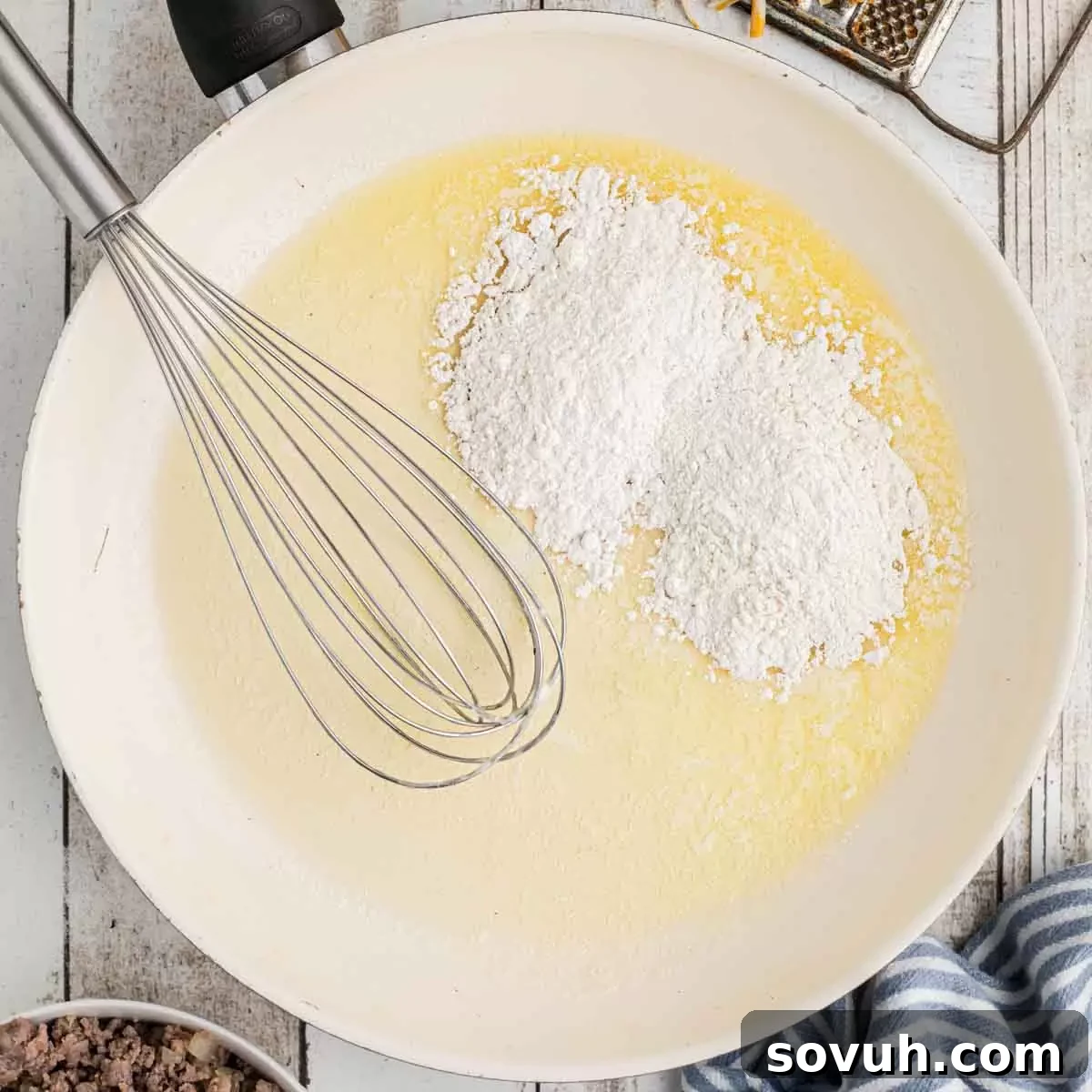 A skillet with melted butter and flour being whisked together to form a roux.