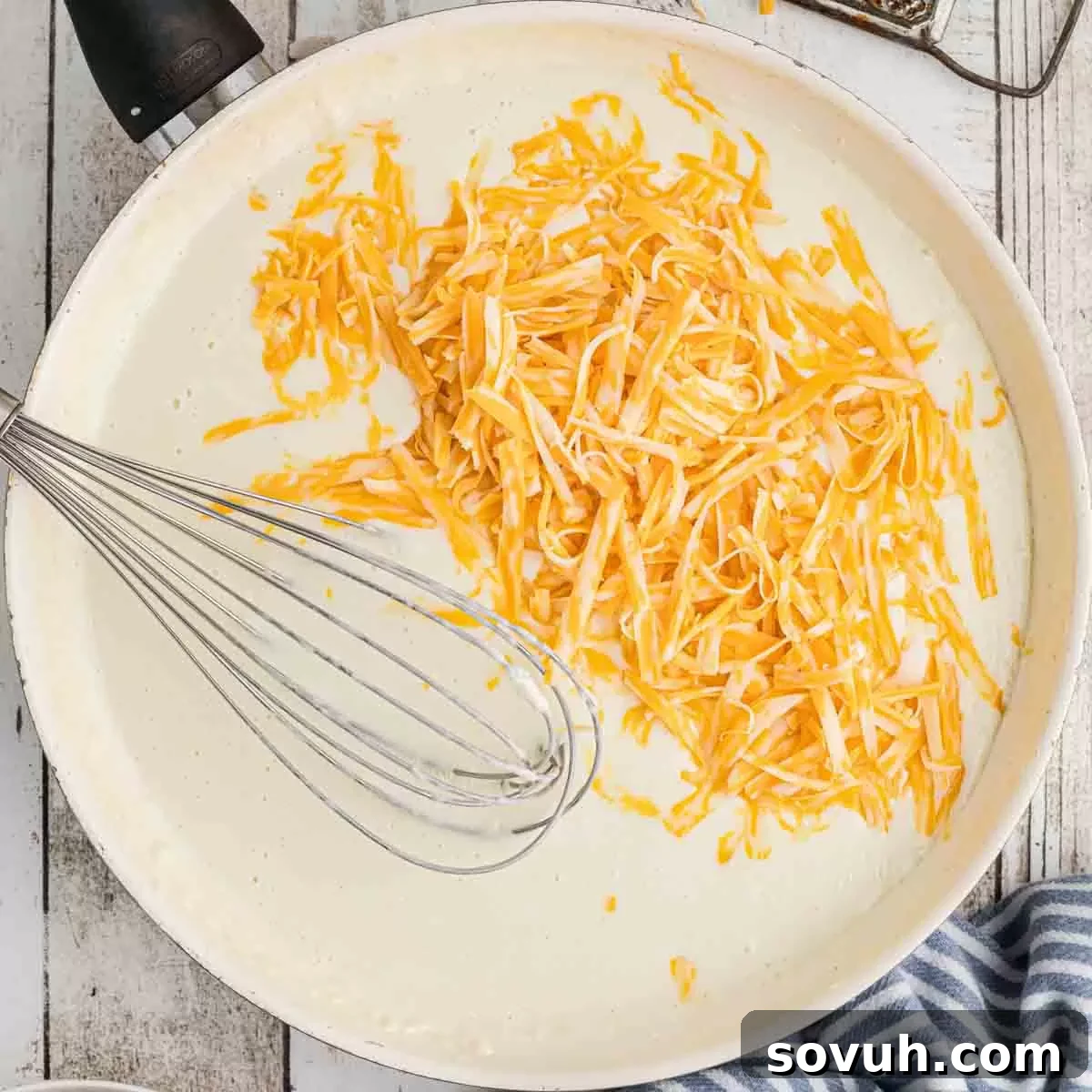 A skillet filled with creamy gravy, with grated cheese melting into it as it's whisked.