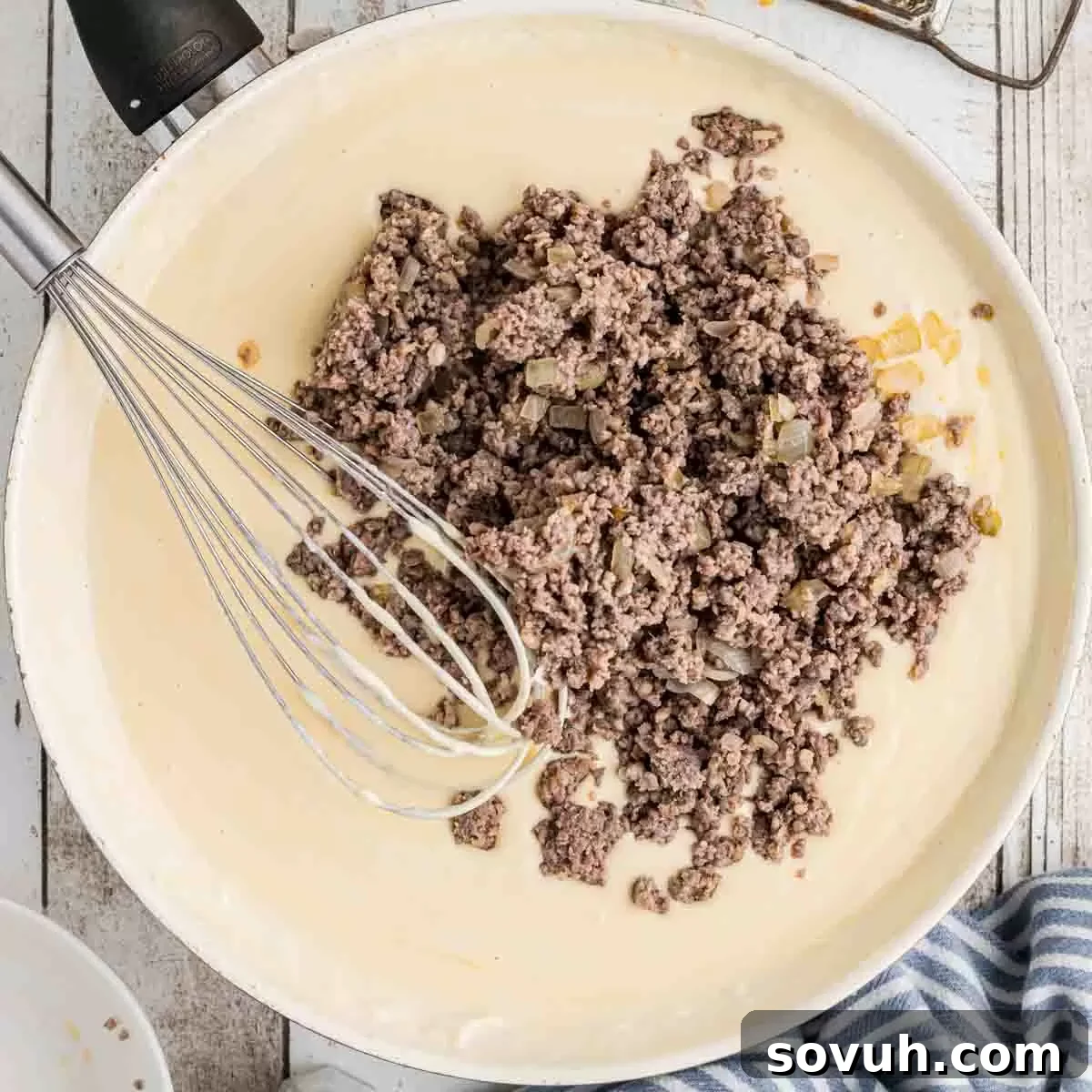 Cooked sausage mixture being stirred back into the creamy cheese gravy in a skillet.