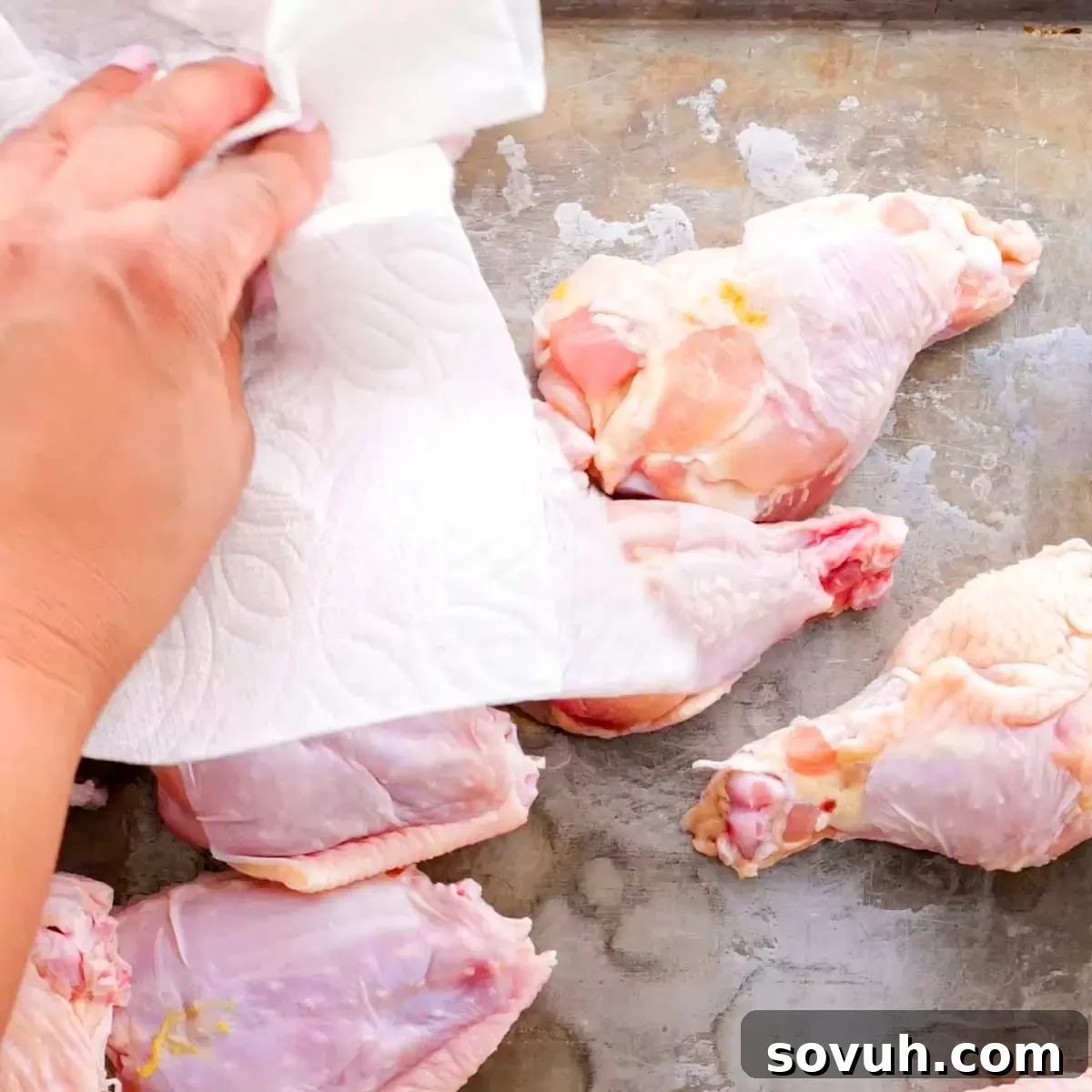 A hand patting dry chicken drumettes on a baking sheet, an essential step for crispy air fryer chicken wings.
