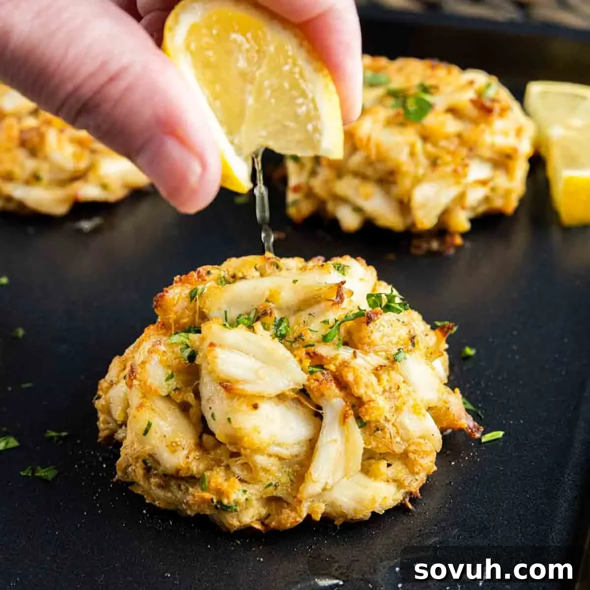 A person drizzling lemon over a batch of Maryland Crab Cakes.