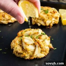 A person drizzling lemon over a batch of Maryland Crab Cakes.