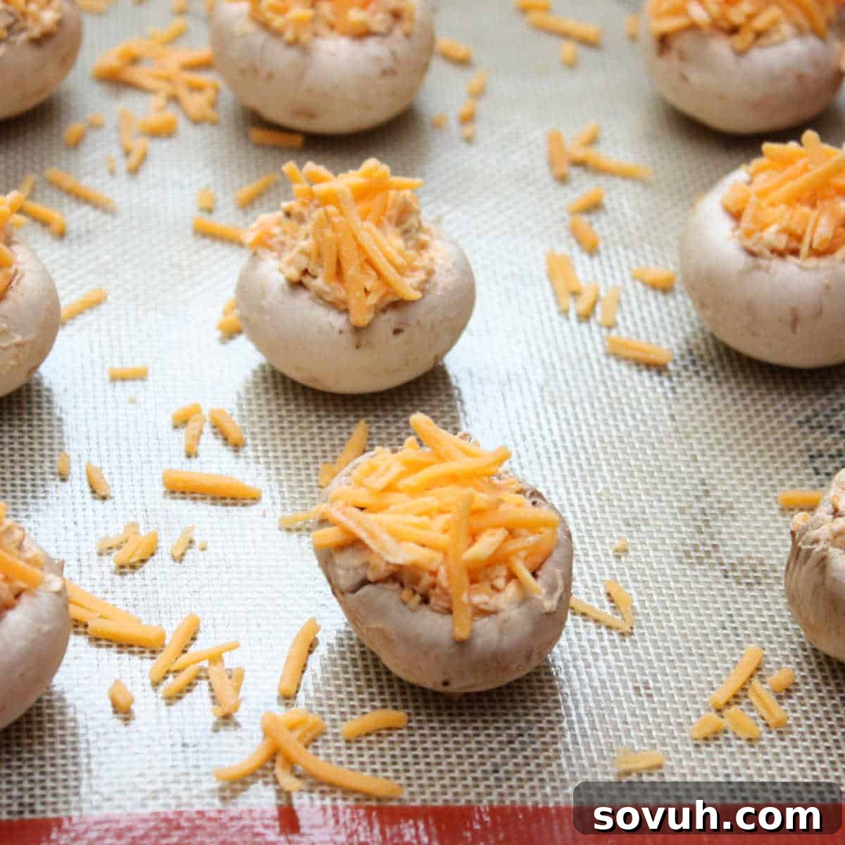 Mushroom caps filled with a stuffing mixture and topped with shredded cheese on a baking sheet.