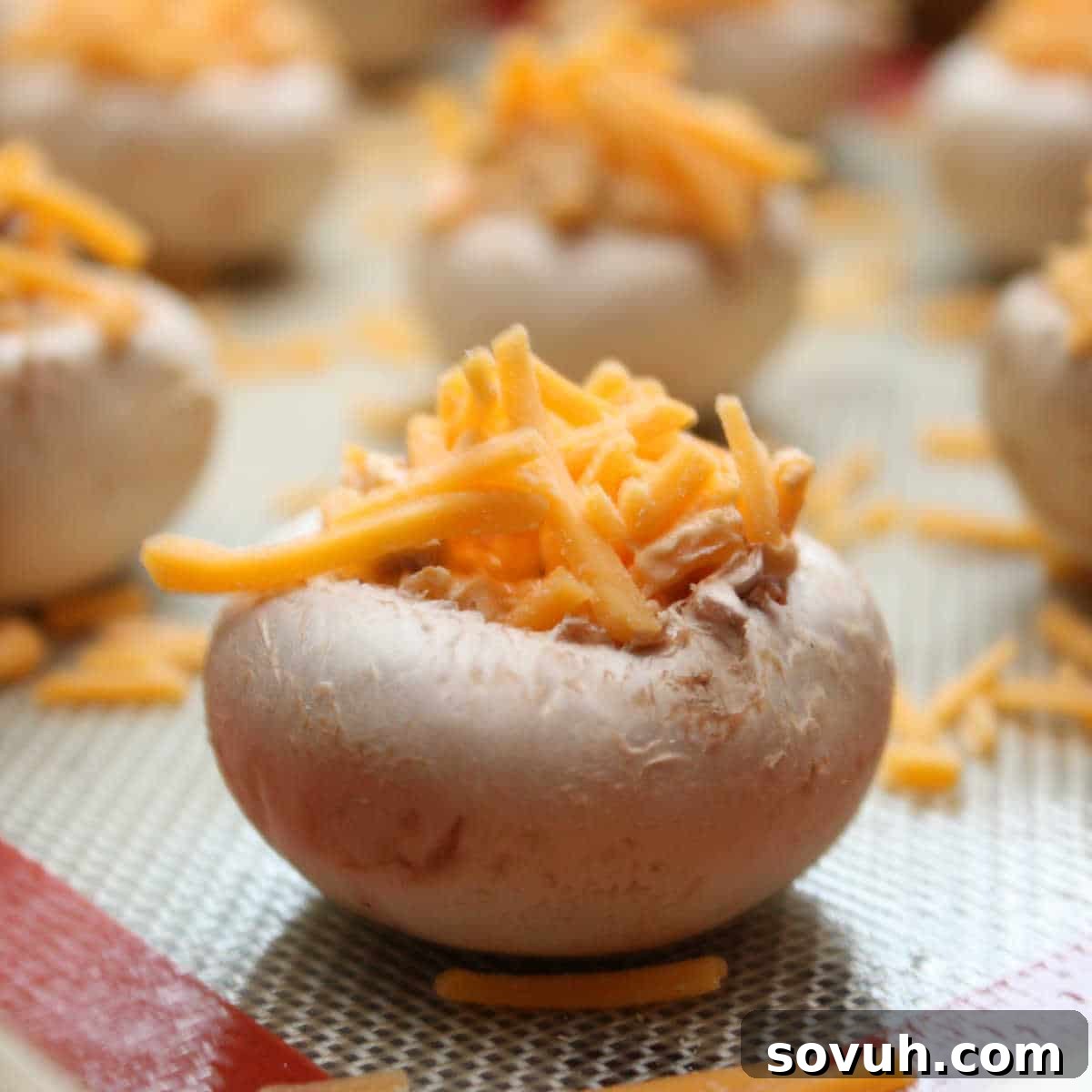 A close-up of a mushroom cap filled with shredded cheese, set on a baking sheet with more mushrooms in the background.