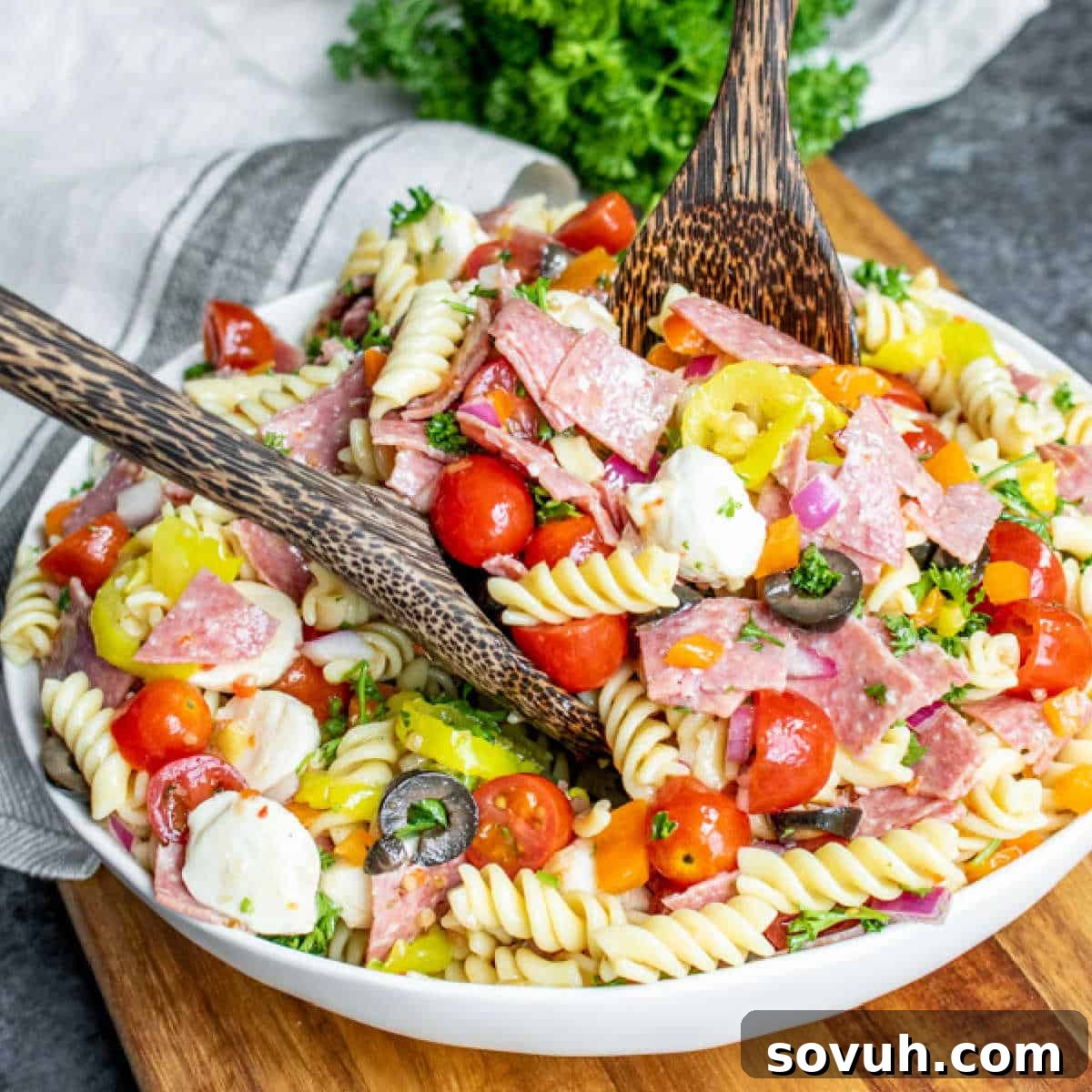 Mastering the Potluck: Unforgettable Dishes for Any Gathering 10 Italian Pasta Salad in a white bowl with wooden serving spoons