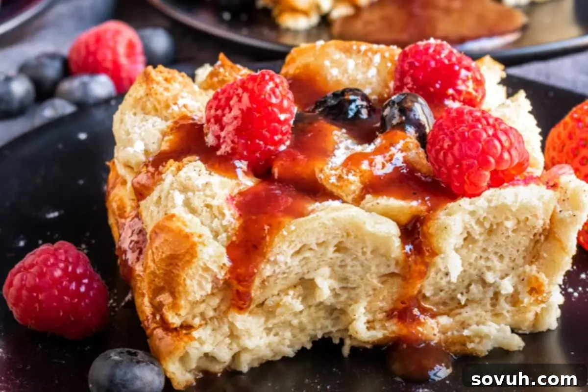A serving of french toast topped with raspberries, blueberries, and drizzled with syrup on a black plate.