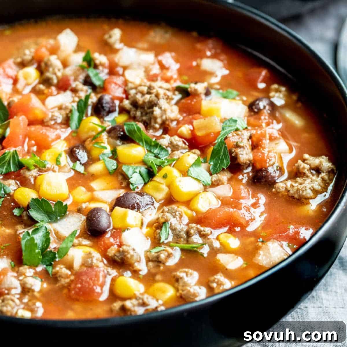 A black bowl brimming with hearty Slow Cooker Taco Soup, garnished with fresh toppings.