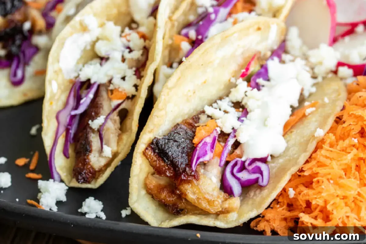 Three gourmet pork tacos artfully arranged with vibrant purple cabbage, finely shredded carrots, and crumbled cheese in soft shells, beautifully presented on a sleek black plate.