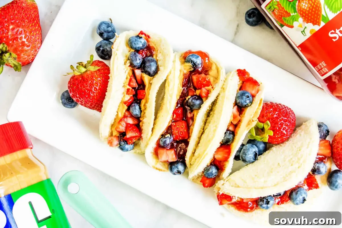 Playful peanut butter and jelly sandwiches, neatly cut into triangles and served alongside fresh, juicy strawberries and plump blueberries on a pristine white plate.