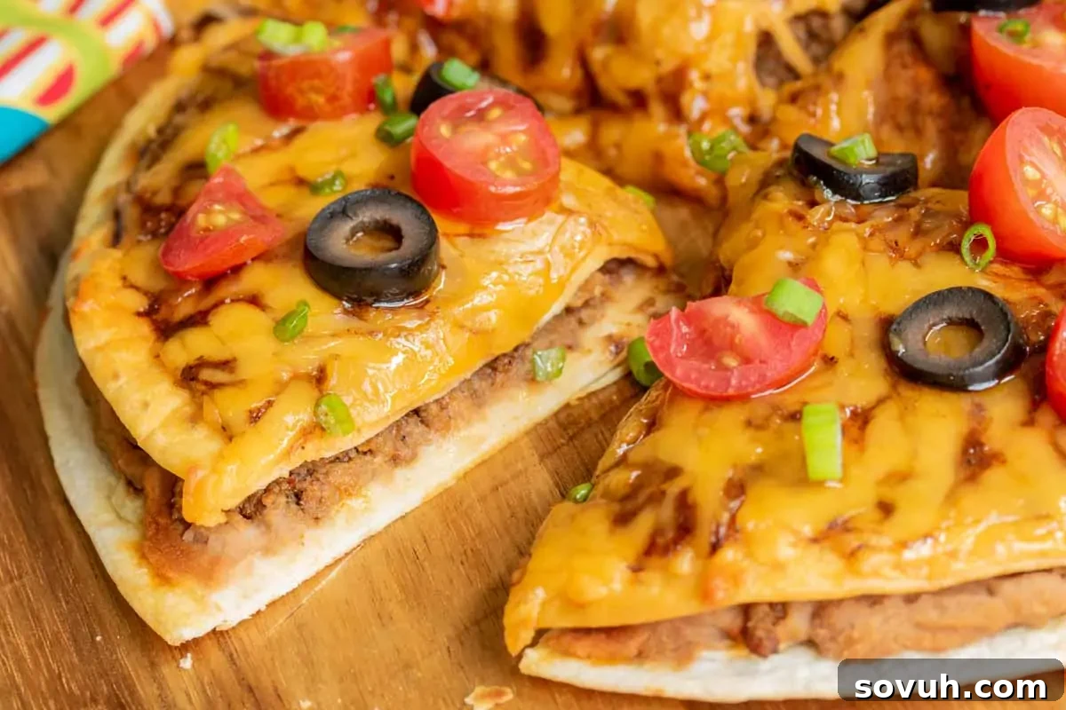 Deliciously sliced cheeseburger pizza topped with halved cherry tomatoes, sliced black olives, and chopped green onions on a rustic wooden board.