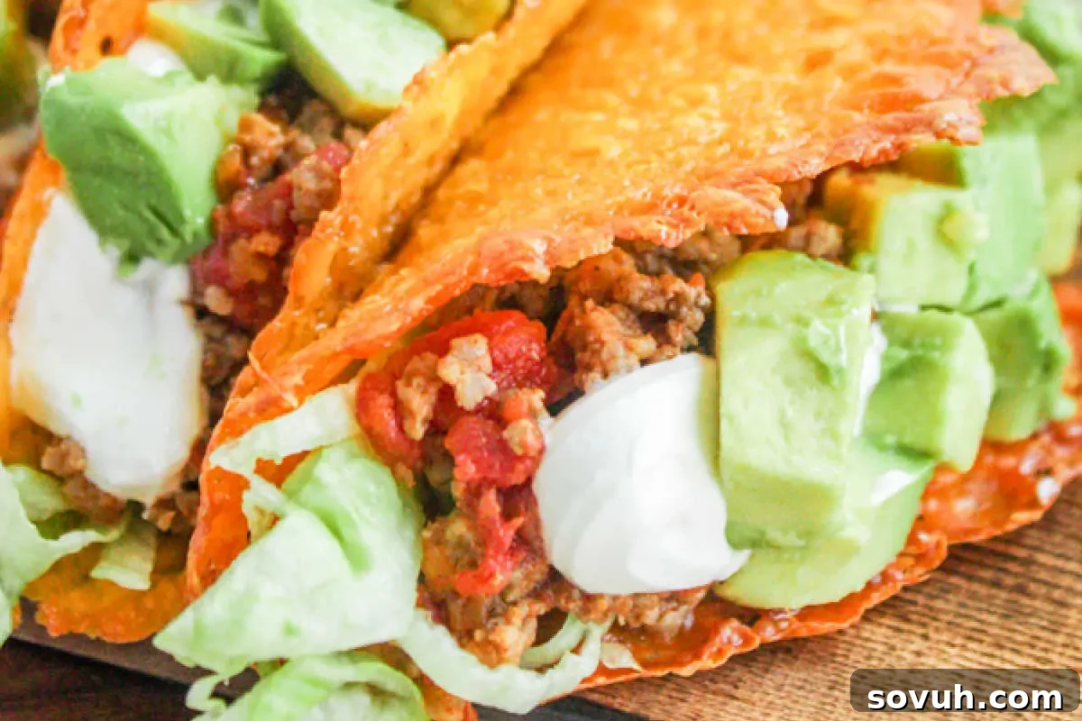 A close-up shot of a delicious taco featuring a crispy cheese shell, generously filled with seasoned ground beef, fresh lettuce, creamy sour cream, and diced avocado, all resting on a rustic wooden surface.