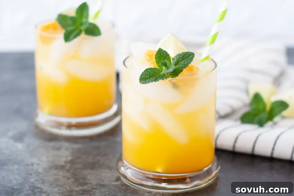 Two glasses of orange juice with ice, garnished with mint leaves and lime slices, accompanied by striped straws on a gray background.