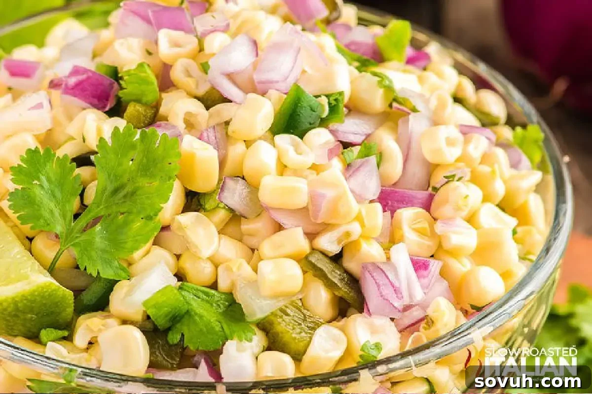 A vibrant bowl of fresh corn salad, beautifully garnished with finely chopped red onion, fresh cilantro leaves, and bright lime slices, showcasing a colorful and appetizing mix of ingredients.