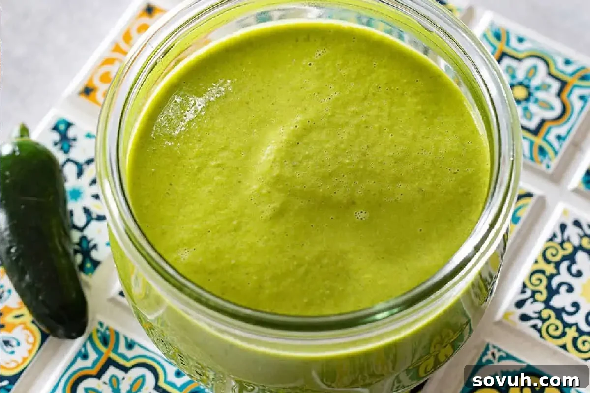 A rustic glass jar filled with vibrant green jalapeño sauce, neatly placed on a decorative ceramic tile coaster, ready to add a kick to any dish.