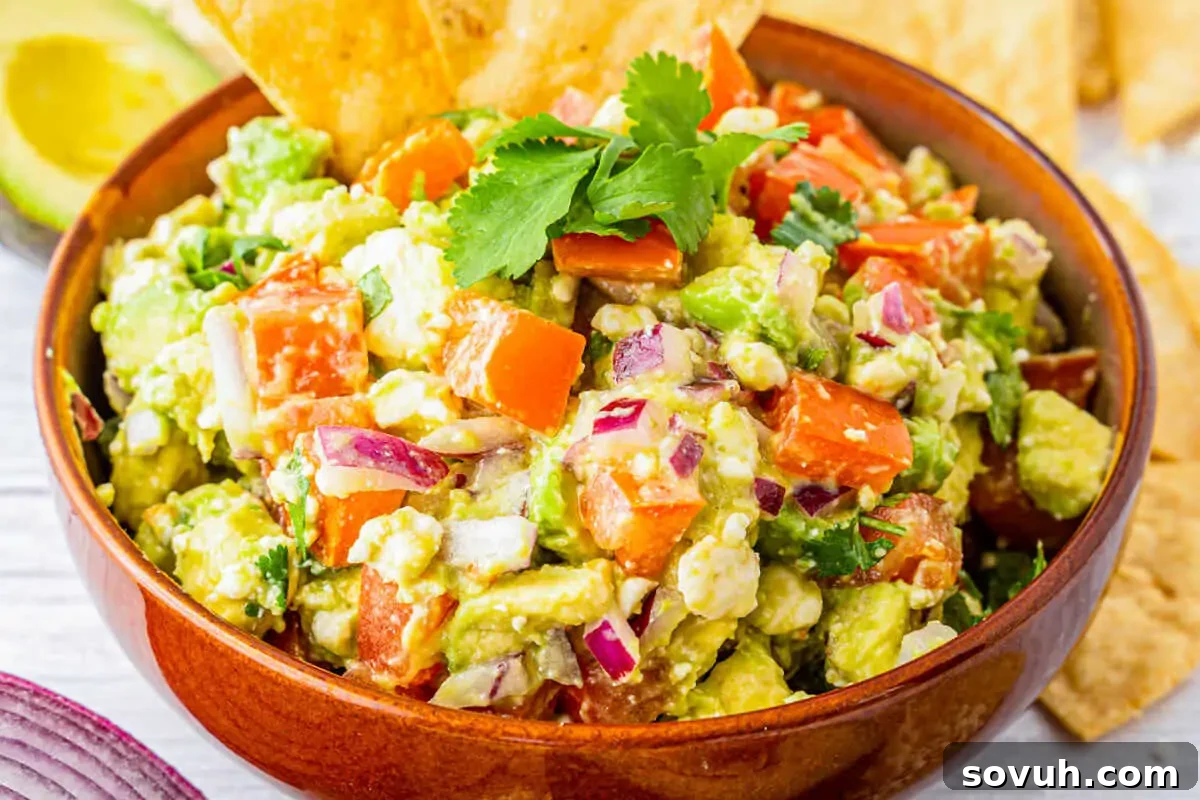 A rustic bowl of chunky guacamole, generously mixed with diced red tomatoes, white onions, and fresh cilantro, served alongside crispy tortilla chips on a wooden table, perfect for sharing.