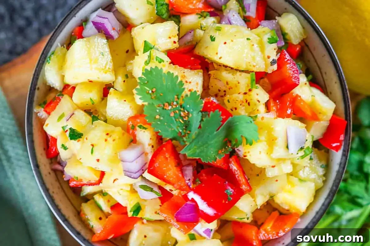 A beautiful bowl of bright yellow pineapple salsa, generously mixed with finely diced red peppers, white onions, and fresh green cilantro, garnished with a sprig of cilantro, ready to be served.