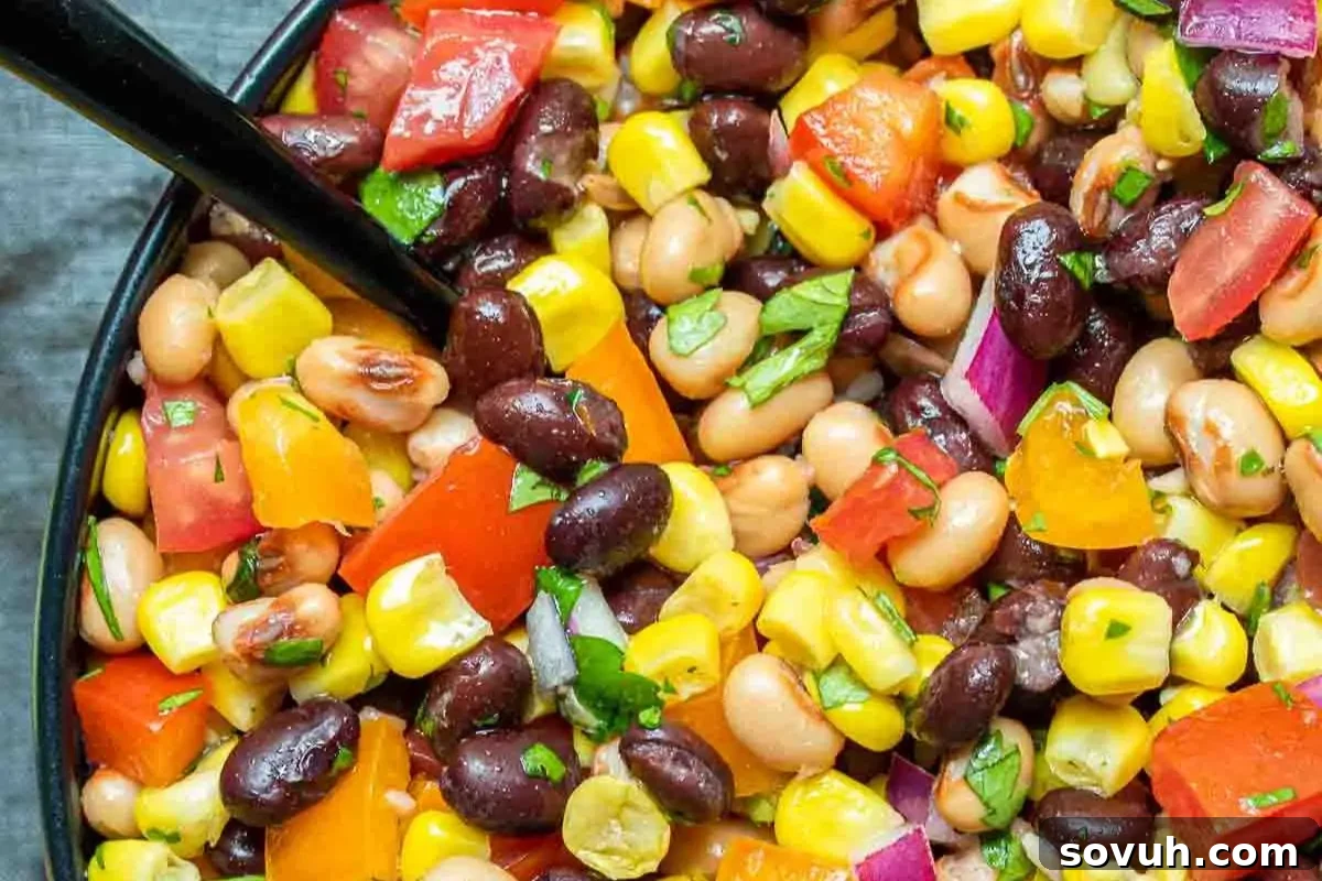 A close-up shot of a vibrant bowl of Cowboy Caviar, bursting with colorful ingredients like black beans, chickpeas, golden corn kernels, diced red tomatoes, and green peppers, served with a black fork, perfect for a Cinco de Mayo celebration.