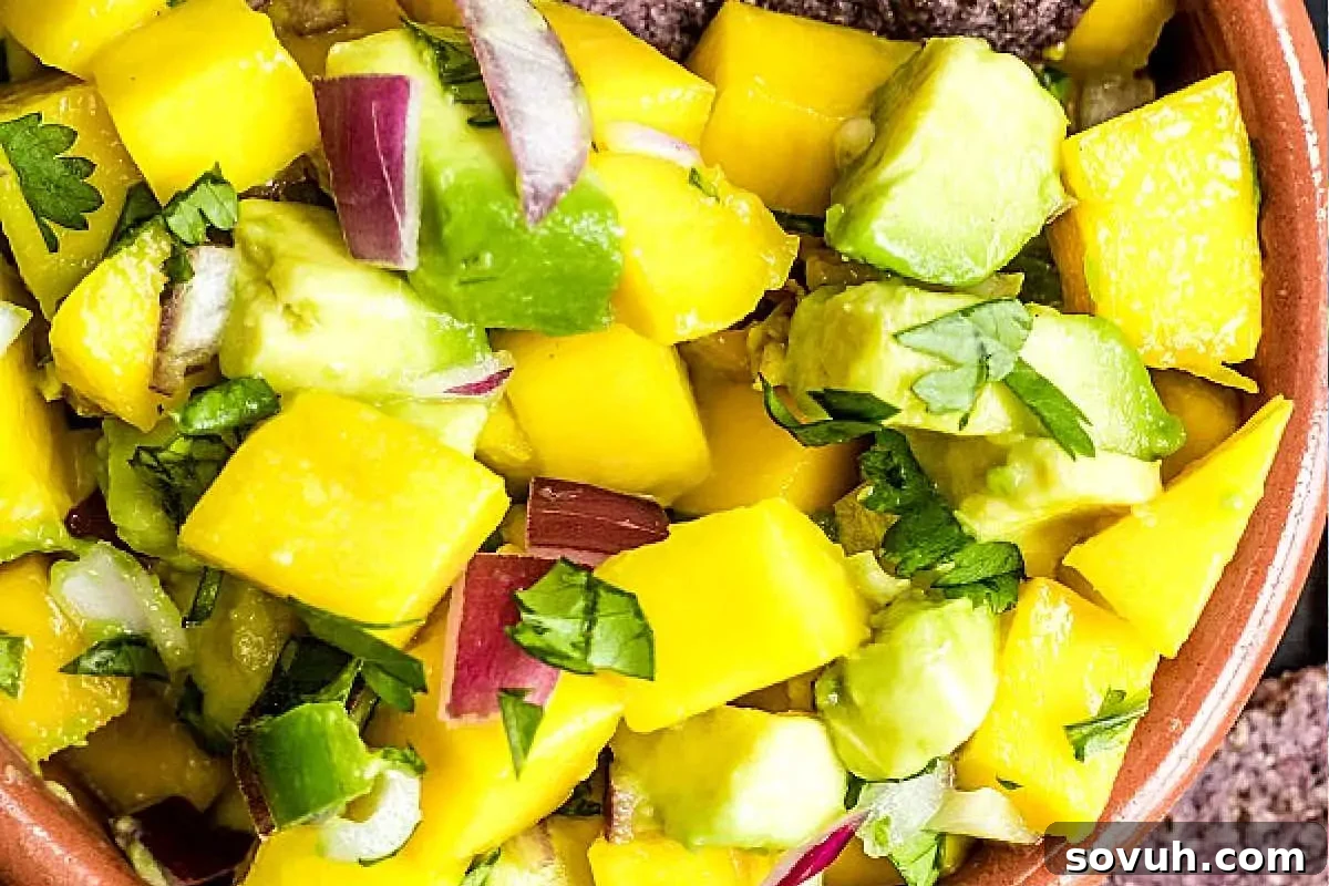 A close-up view of a fresh and colorful mango avocado salsa served in a bowl, featuring perfectly diced mango, creamy avocado chunks, finely chopped red onion, and vibrant cilantro leaves, creating a delightful texture and flavor.