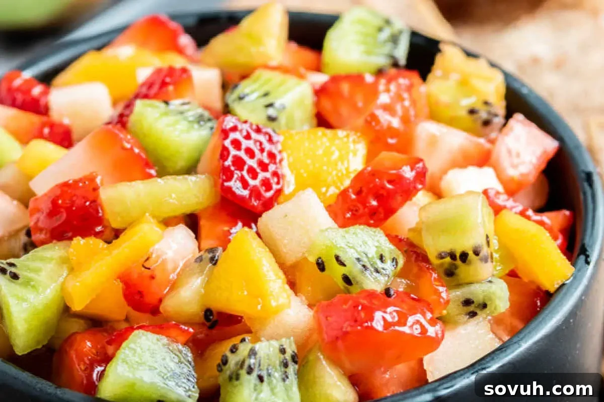 A close-up shot of a vibrant and colorful mixed fruit salad, featuring diced strawberries, bright kiwi slices, juicy orange segments, and other fresh fruits, beautifully presented in a black bowl, perfect for a refreshing treat.