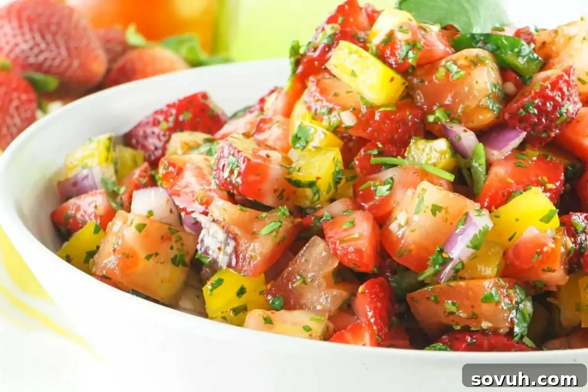 A vibrant bowl of strawberry tomato salsa, finely chopped with red onions, fresh herbs, and peppers, creating a colorful and fresh dip.