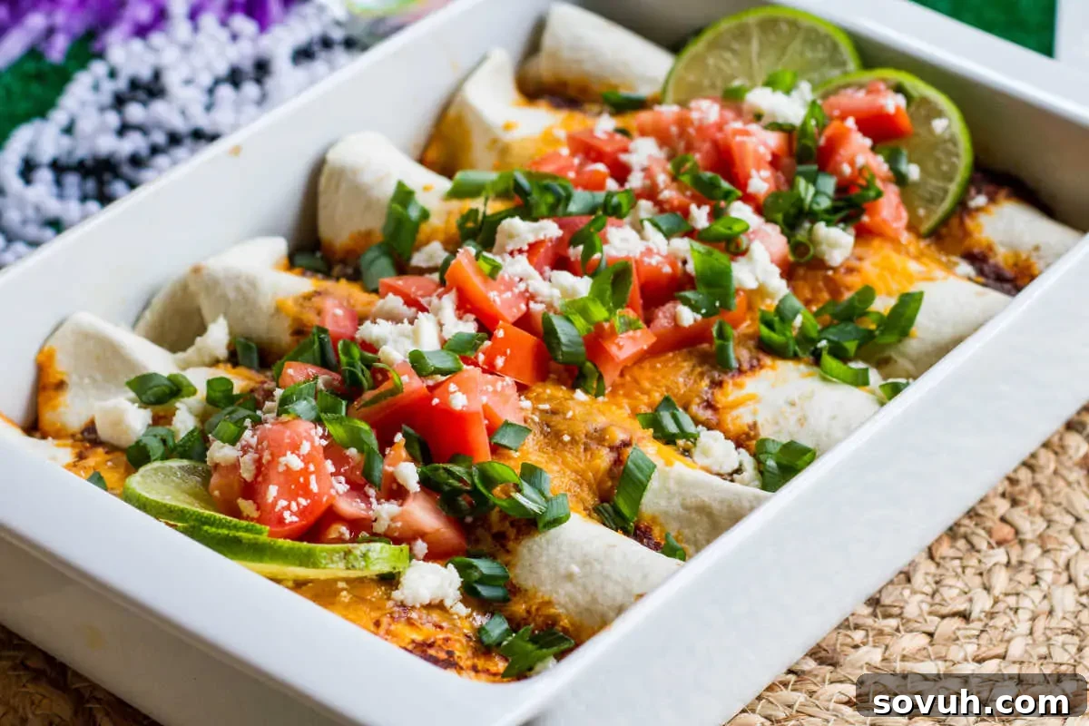 A tray of enchiladas topped with cheese, diced tomatoes, green onions, and lime wedges, served on a woven placemat.