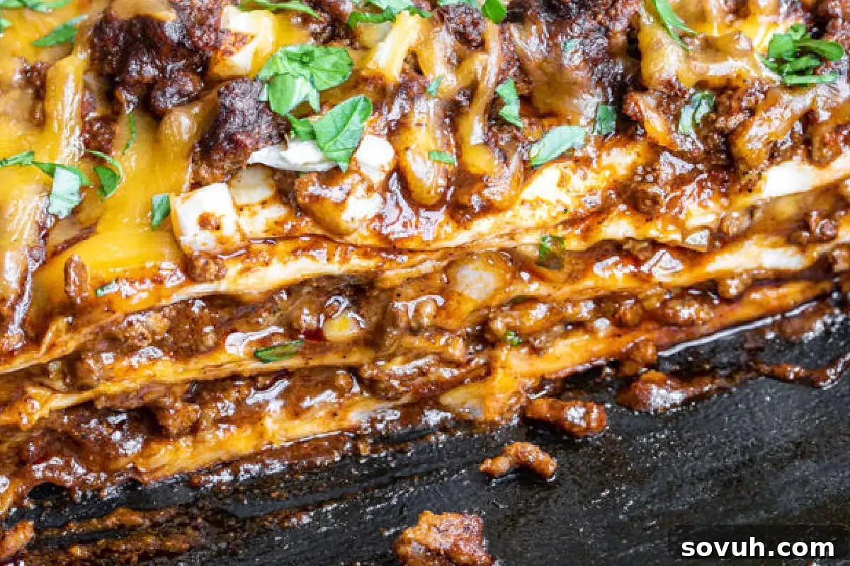 Close-up image of a layered lasagna with melted cheese and meat sauce, garnished with chopped herbs.