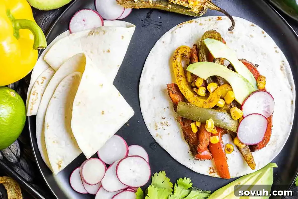 Festive open tortilla with sautéed vegetables, avocado slices, and radish, accompanied by lime wedges and cilantro on a black plate.