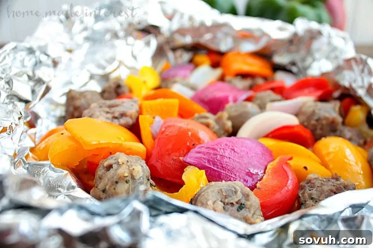 Grilled foil packets containing sausage meatballs and mixed bell peppers in vibrant colors of yellow, orange, and red, with onions, served on a plate.