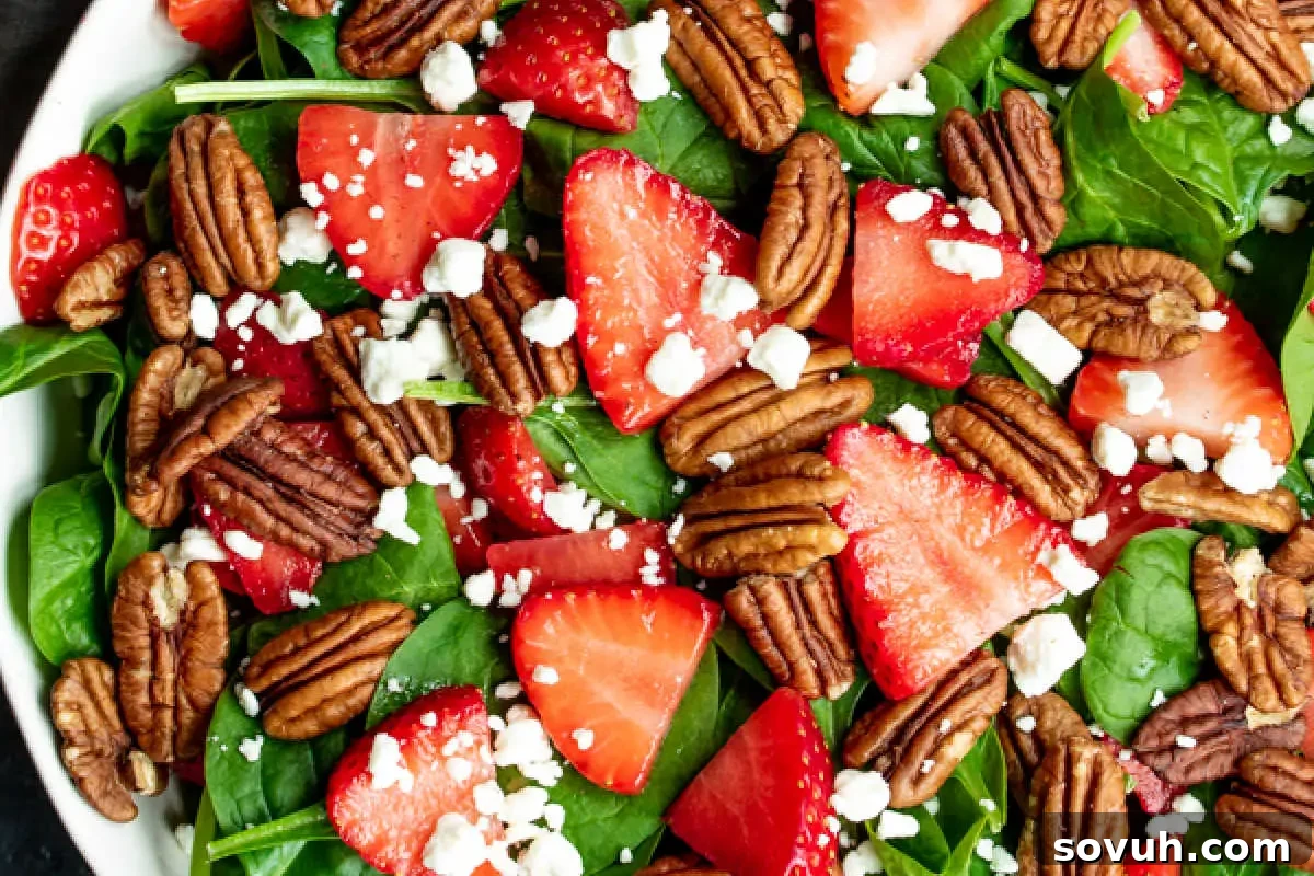 A fresh spinach salad topped with strawberries, pecans, and crumbled feta cheese, served in a black bowl.