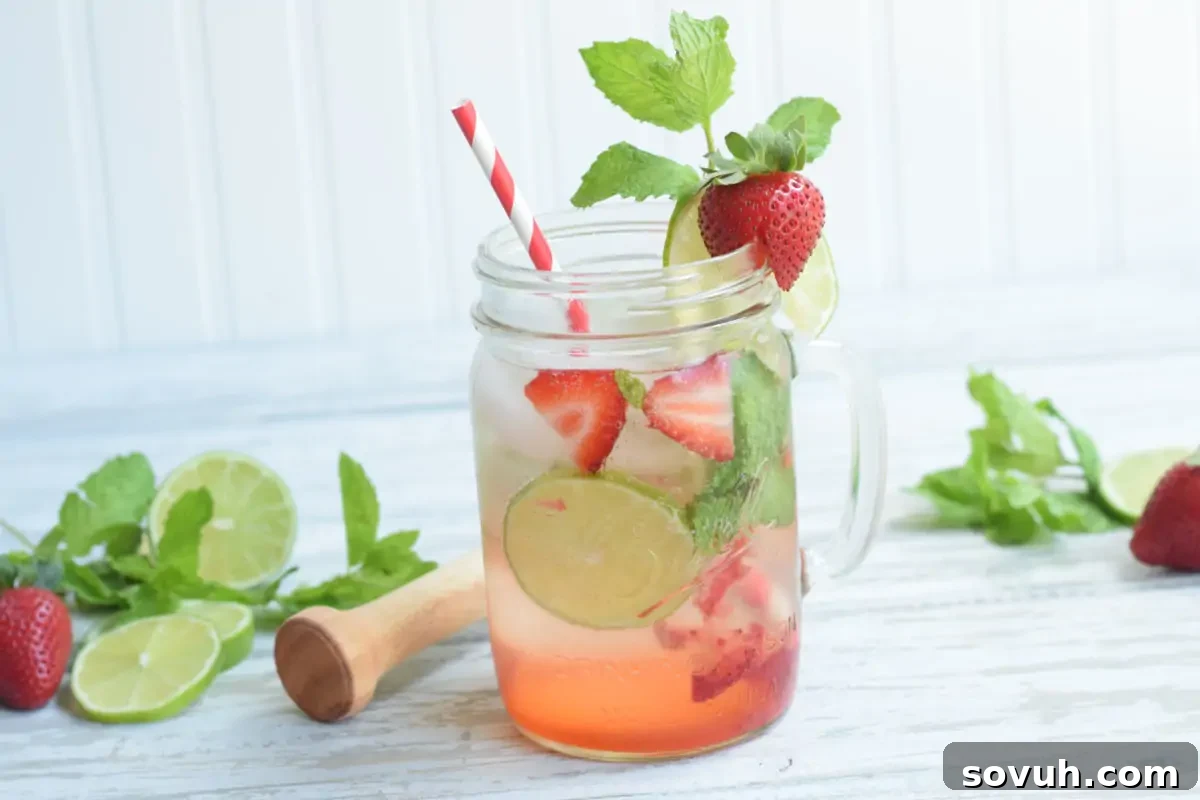 A refreshing strawberry lime drink in a mason jar with a striped straw, surrounded by fresh strawberries, lime slices, and mint leaves on a wooden surface.