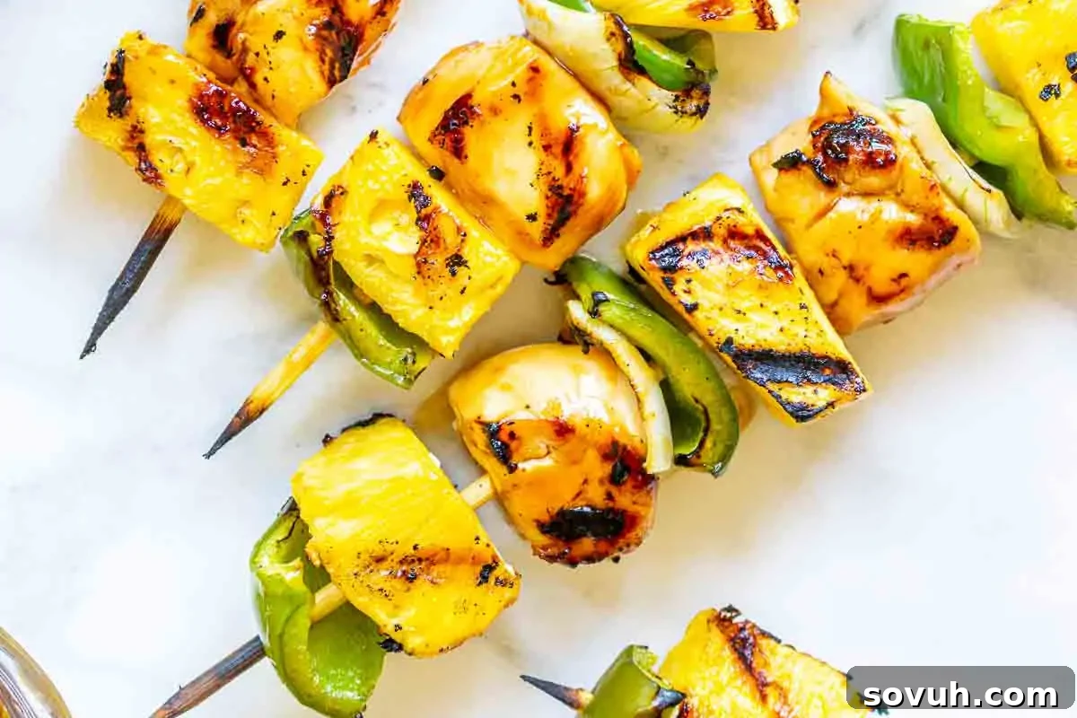 Grilled skewers with pineapple, green bell peppers, and onions on a white marble surface.